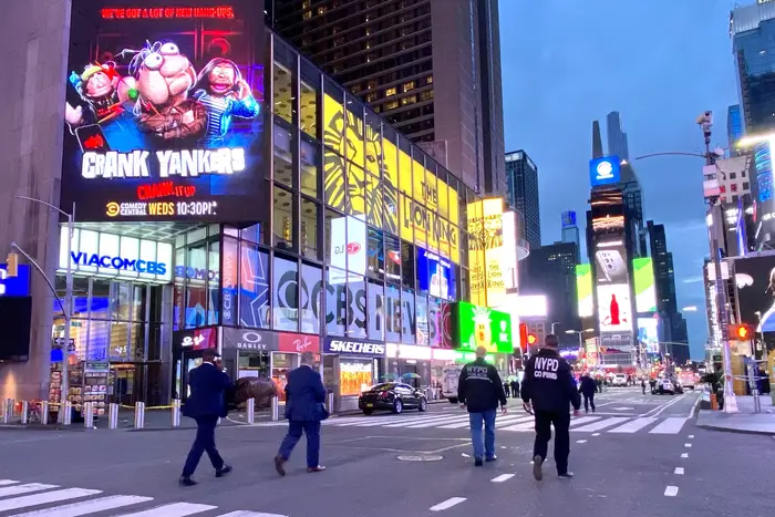 Four members of the NYPD walk in the empty Times Square streets towards the crime scene on 7th Avenue between 44th and 45th; the streets were cleared for the response, and the billboards and marquees are shining brightly